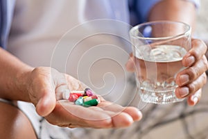 Asian old man taking in pill and another hand holding a glass of clean mineral water. Senior healthcare and medicine concept