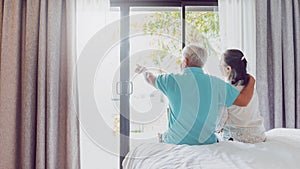 Asian old senior couples talking and sitting on bed in hotel room background on weekend vacation.Concept of happy living for the