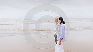 Asian old senior couples walking at the beach by the sea background on weekend vacation.Concept of happy living for the elderly