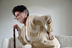 Asian old woman sitting on sofa and having a back pain, backache at home. Senior healthcare concept