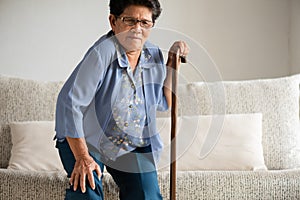 Asian old woman sitting on sofa and having knee pain, knee injury at home. Senior healthcare concept