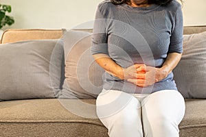 Asian old woman sitting on sofa with stomach ache irritable bowel syndrome Abdominal pain in the elderly, flatulence,