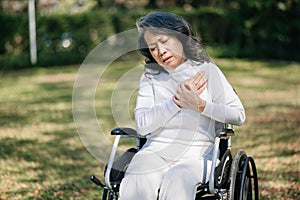 Asian old woman sitting on a wheelchair outdoors in the park Have pain in the arms, wrists and body in sun light