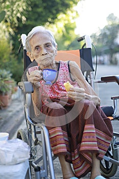 asian old woman sitting on whell chair and drinking warm beverage