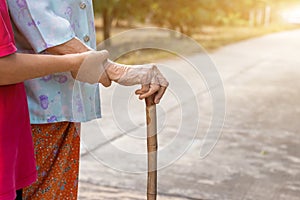 Asian old woman standing with her hands on a walking stick ,Hand of old woman holding a bamboo cane stick for helping walking