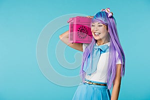 Asian otaku girl in purple wig holding boombox isolated on blue