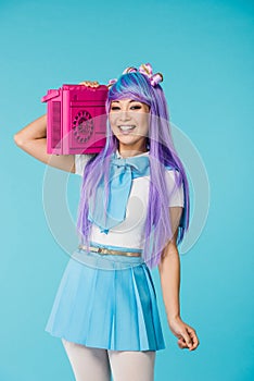 Asian otaku girl in purple wig holding boombox isolated on blue