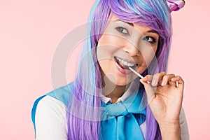 Asian otaku girl in wig eating lollipop isolated on pink
