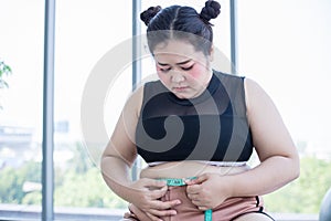Asian overweight woman measuring fat layer with waistline at home