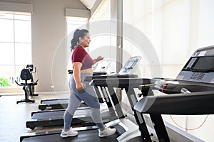 Asian overweight women in sportswear running on treadmill in fitness club. Weight loss workout, healthy lifestyle concept