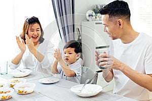 Asian parents clapping hands and giving compliment as their child does good job while having meal together at home.
