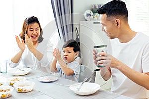 Asian parents clapping hands and giving compliment as their child does good job while having meal together at home. photo