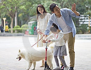 Asian parents & daughter playing scooter while walking dog in garden