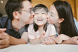 Asian Parents kissing their little daughter on both cheeks. family portrait.