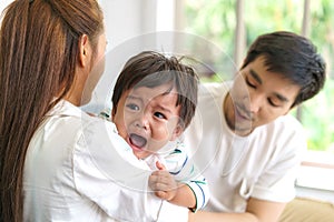 Asian Parents with mother and father trying to calm down crying infant son in living room at home