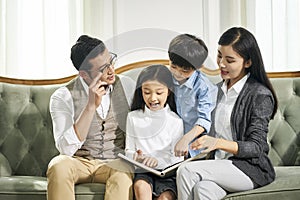 Asian parents and two children reading book together