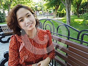 Asian park woman sitting on bench smiling happy at camera. Pretty young multiethnic woman enjoying summer in park