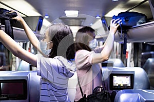 Asian passenger stowed her backpacks in a overhead storage on the tour bus,people wearing protective masks to safety from the photo