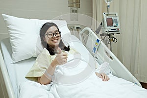 Asian patient girl thumbs up and smile while lying on hospital bed