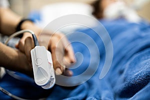 Asian patient`s hand with an attached pulse oximeter on finger for monitoring,daughter holding her mother`s hand,supporting