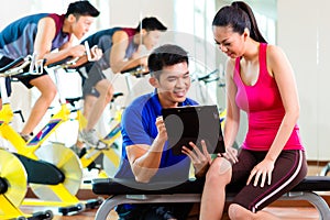 Asian personal trainer with woman in fitness gym