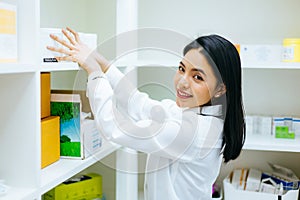 Asian pharmacist doctor in white gown checking medical health stock products and working in drugstore in shop.