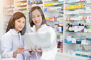 Asian pharmacist female using laptop computer and checklist inventory or reading information medication in pharmacy or drugstore.