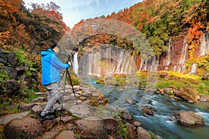 Asian photographer taking landscape photos of waterfall. Fall foliage in autumn season near Fujikawaguchiko, Yamanashi. Trees in