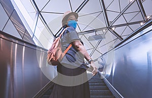 Asian plus size female passenger in protective mask looking back at camera while going up on escalator at subway station