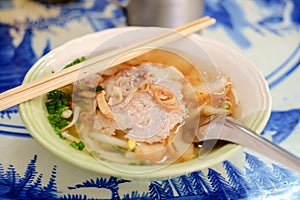 Asian pork noodle soup in a bowl with short spoon and wooden chopsticks