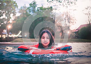 Asian pre teen girl swimming in a floating ring in resort swimming pool in orange swimwear