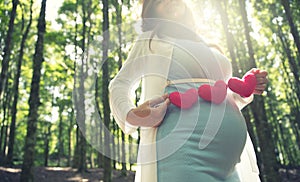 Asian pregnant woman in blue dress in the florest background holding heart shape accessories