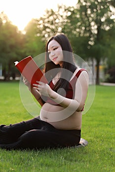 Asian pregnant woman Chinese read red cover book sit on grass lawn in nature outdoor sunshine sunset sunrise day enjoy peaceful