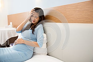 Asian pregnant woman has headache sitting on her bed