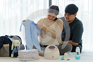 Asian Pregnant woman and her husband prepare baby monitor utensils, container preparation for pregnancy concept in bedroom at home