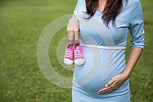 Asian pregnant woman holding a pair of pink toddler shoes