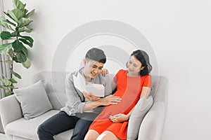 Asian pregnant woman and husband sitting on sofa and reading book