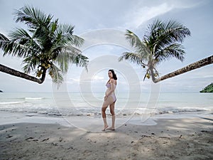 Asian pregnant woman posture on tropical sand beach with palm tree in sunny day in Thailand. Pregnancy relaxation from depression