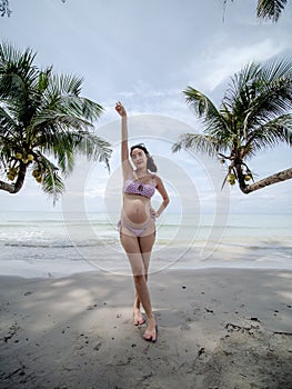 Asian pregnant woman posture on tropical sand beach with palm tree in sunny day in Thailand. Pregnancy relaxation from depression