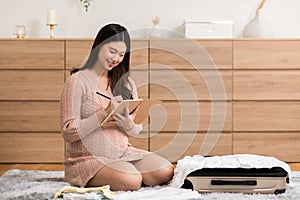 Asian pregnant woman preparing diaper, feeding bottle for baby at home. Pregnant woman packing baby stuff ready for the maternity