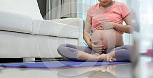 Asian Pregnant Woman in sitting touching her belly while doing yoga exercise