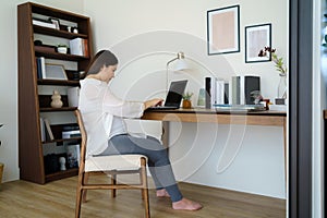 Asian pregnant woman  using a laptop while working on maternity leave at her living room table at home