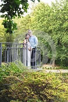 Asian pregnant women and caucasian husband standing near iron railings in park