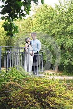 Asian pregnant women and caucasian husband standing near iron railings in park