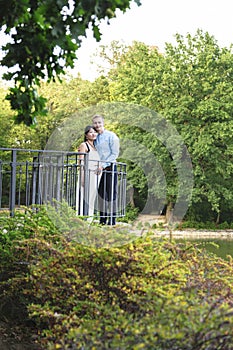 Asian pregnant women and caucasian husband standing near iron railings in park
