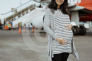 Asian pregnant women standing beside a suitcases on the runway