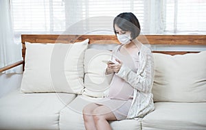 Asian pregnant women wearing medical mask due to illness, dizziness using smart mobile phone with worry, pandemic Wuhan