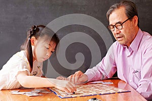 An Asian preschool girl learning to play board games with her grandfather