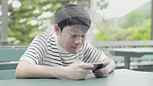 Asian preteen boy playing game on mobile near road with excite face.