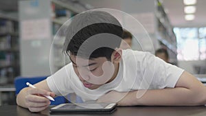 Asian preteens boys using tablet computer at library .